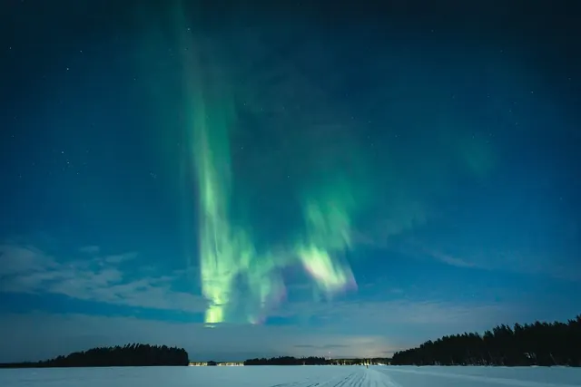 Revontulet jäätyneen järven ja metsän yllä