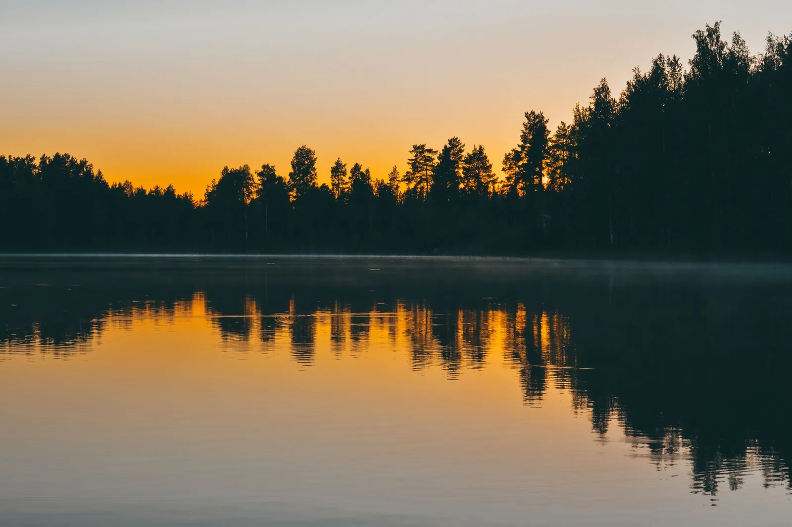 Auringonlasku metsäisen järven yllä
